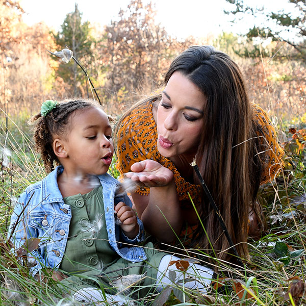 Family photographer - a woman and her daughter blow flowers in a field
