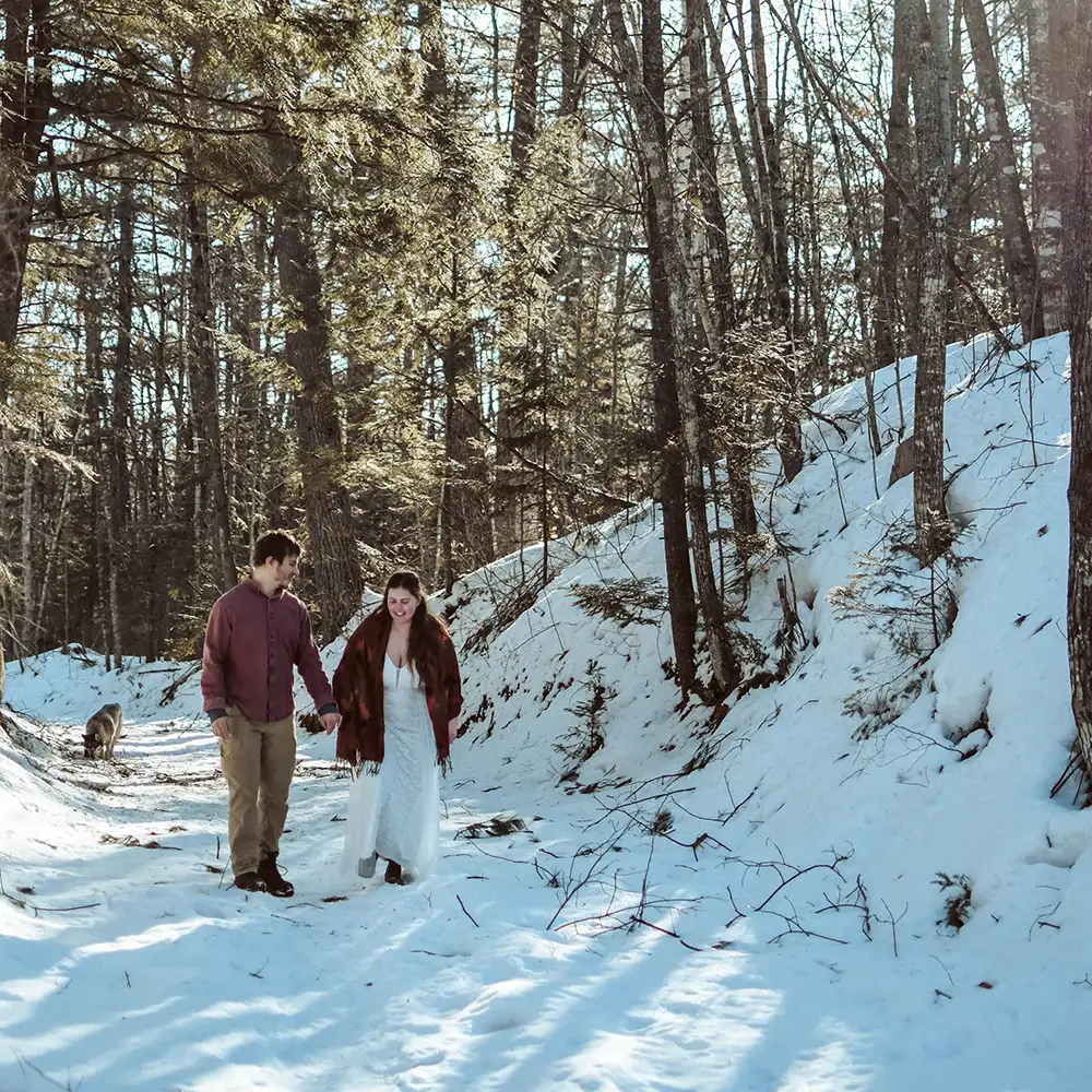 A couple walk in snowy woods, holding hands, after they have eloped