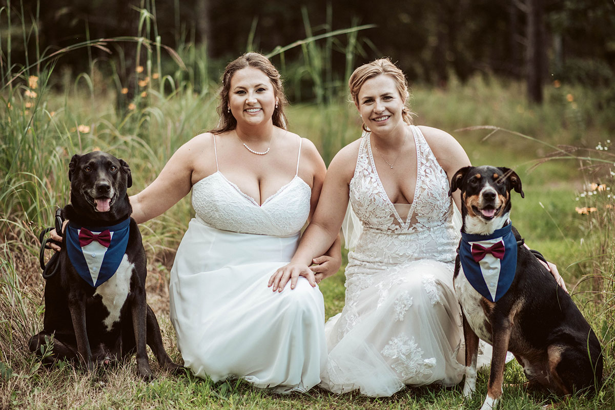 Two brides pose for a photograph with their dogs.