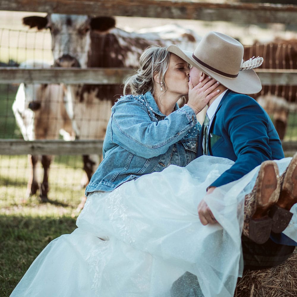 A couple kiss in front of a cow during their outdoor wedding