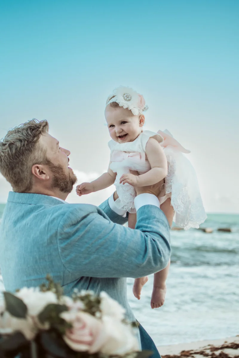 The groom holds up his baby daughter while she laughs