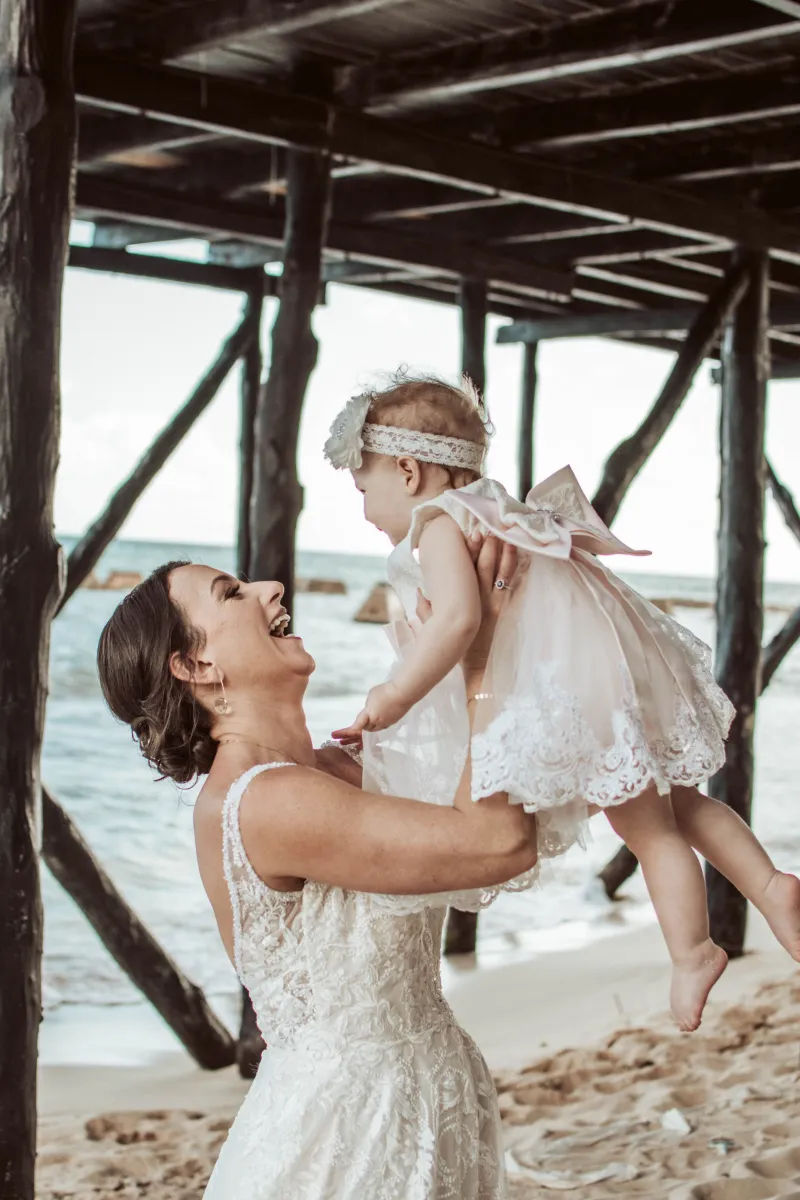 Bride holds her daughter up in the air, with a huge smile on her face