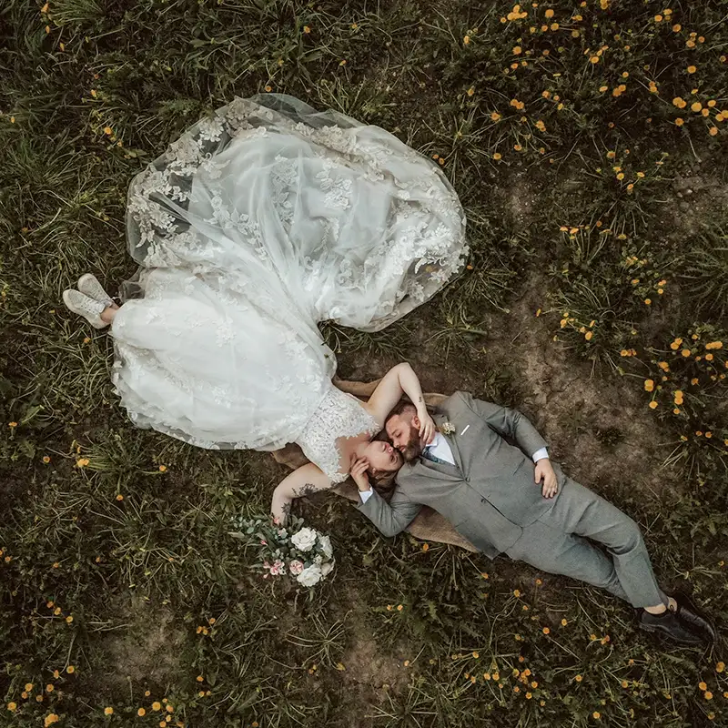 An aerial photograph of a bride and groom lying on the grass, taken using a drone